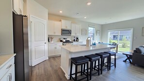 A modern kitchen with white cabinetry, a central island with stools, a microwave, and a stove. - New 2025 Beach Home! Ocean View Beach Club! 5 Minutes to Bethany Beach (Ocean View)