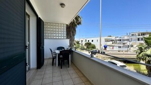 Ein Balkon mit Tisch und Stühlen, Fliesenboden, einer gemusterten Wand und Blick auf Gebäude sowie eine Palme.