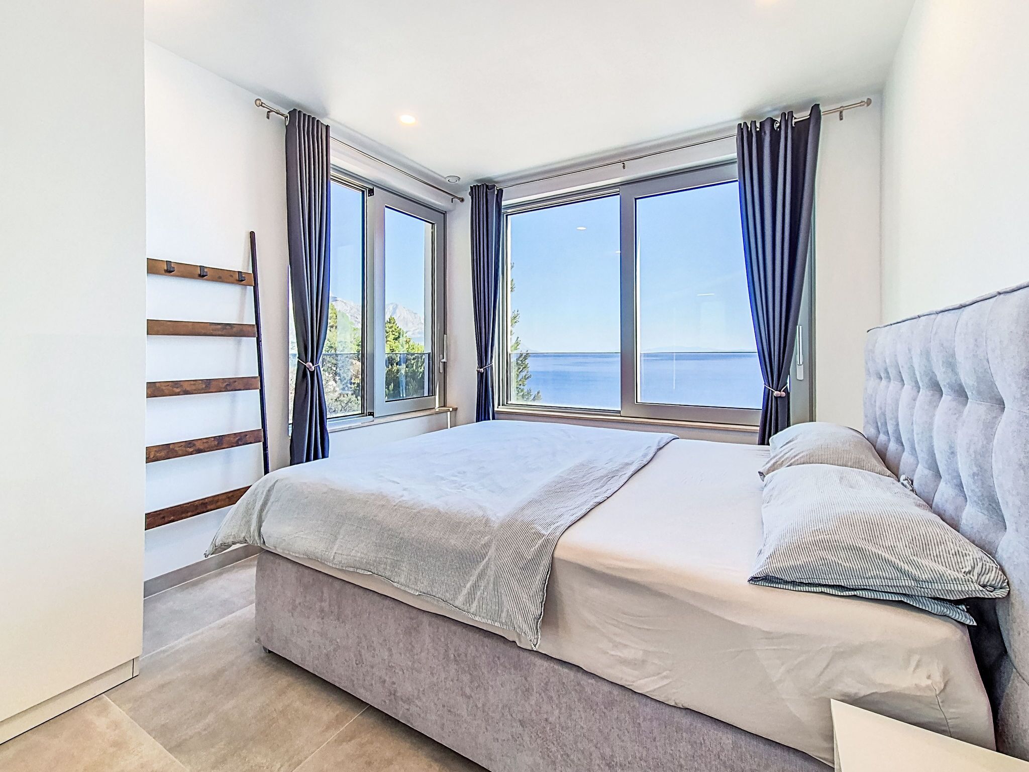 A bedroom with a bed, large windows, and a view of the sea.