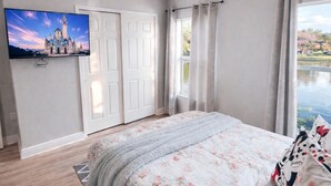 Un dormitorio con cama, ventilador de techo, televisor en la pared y vista a un lago.