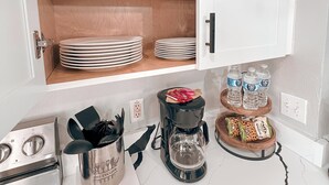 Una cocina con cafetera, jarra de café y una repisa con platos y tazas.