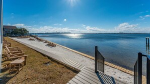Una playa con muelle de madera, sillas de descanso y vista despejada al agua.