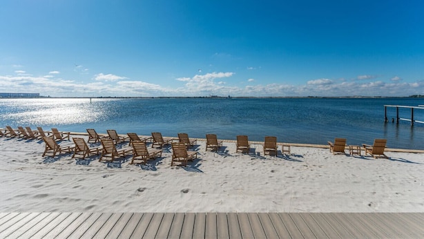 Una playa con sillas de madera dispuestas sobre la arena, una terraza de madera y una vista despejada del mar.