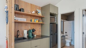 A compact kitchen with wooden shelves, a coffee machine, and a refrigerator.