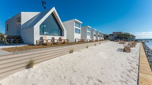 A beachfront hotel with a modern design, featuring a wooden boardwalk leading to the beach, and multiple rooms with large windows.