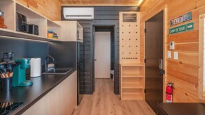Une cuisine moderne avec un plan de travail noir, une machine à café et un évier. On y trouve une porte en bois sur laquelle est apposée une plaque portant l’inscription : « Dwells Beyond the Ordinary » (en français : « Un lieu qui sort de l’ordinaire »).