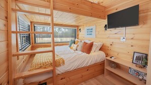 Une chambre de style cabane en bois avec un lit superposé, un téléviseur fixé au mur et une fenêtre avec des stores.