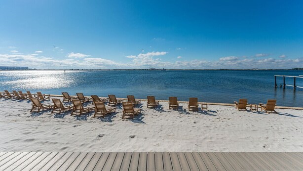 Une plage avec des chaises longues en bois disposées sur le sable, une terrasse en bois et une vue dégagée sur la mer.
