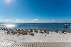 Ein Strand mit Holzliegen, die im Sand angeordnet sind, eine Holzterrasse und freie Sicht auf das Meer.