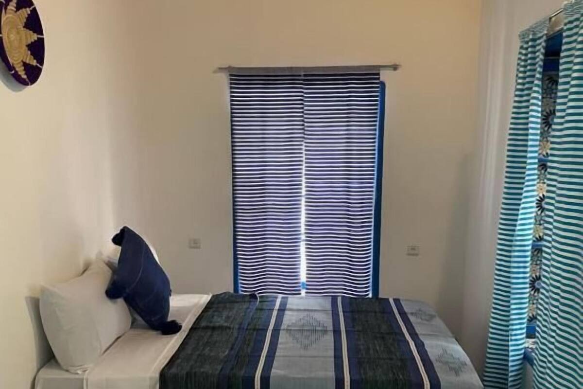 Habitació petita i acollidora amb un llit, un sofà i una finestra amb persianes estriades.