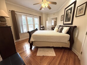 A bedroom with a bed, wooden floor, ceiling fan, and a window with curtains.
