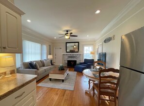 A spacious living room with a fireplace, a dining area with a table and chairs, and a kitchen with a refrigerator.
