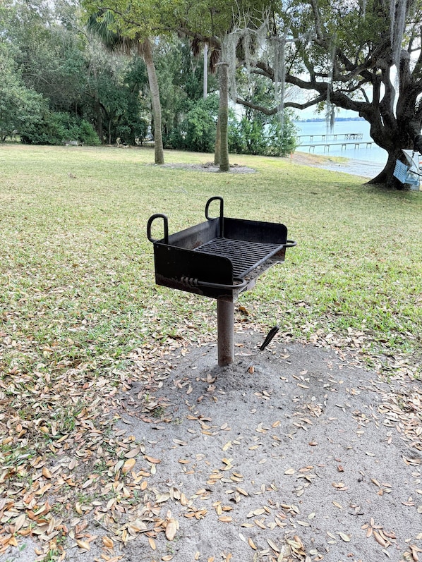 Una parrilla de barbacoa en un parque con árboles y un lago al fondo.