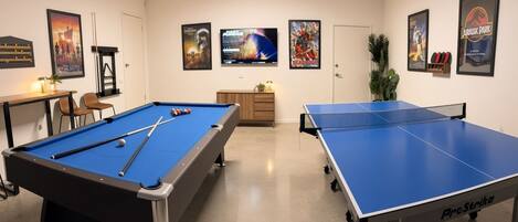 Une salle de loisirs équipée d’une table de billard, d’une table de ping-pong et de posters aux murs.