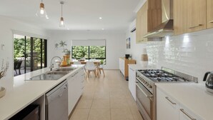 Una cucina moderna con mobili bianchi, piano cottura a gas e lavastoviglie. È presente un'area pranzo con tavolo e sedie, e una finestra che offre luce naturale.