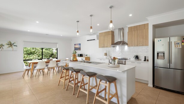 Una cucina moderna con isola centrale, sgabelli da bar, mobili in legno, elettrodomestici in acciaio inossidabile e un'ampia finestra con vista sul verde.