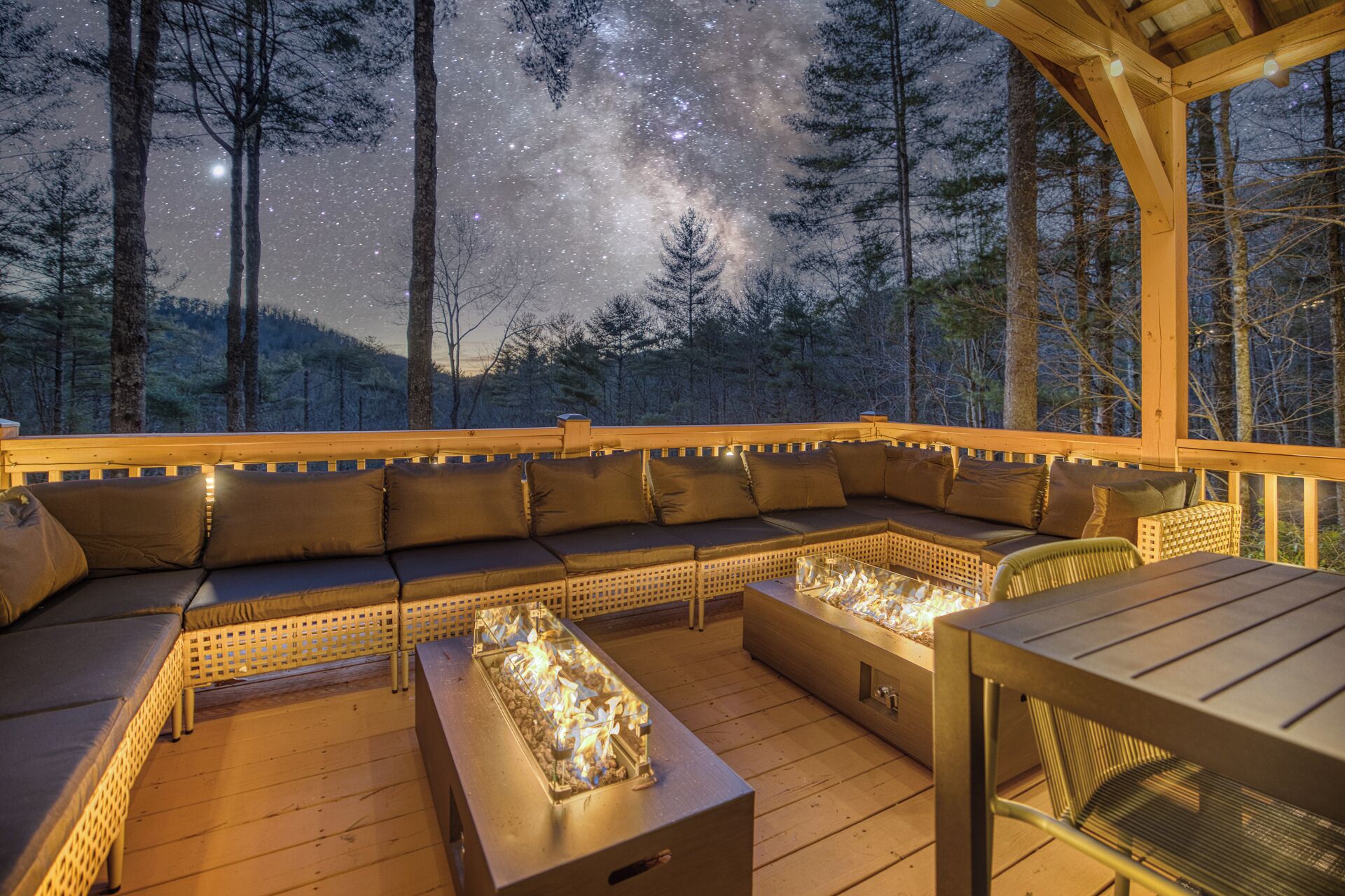 An outdoor deck with a built-in sofa and a fire feature, surrounded by trees and a starry night sky.
