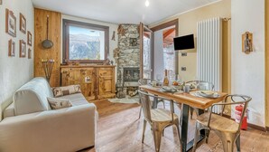 A cozy living room with a fireplace, wooden furniture, and a dining area with a table and chairs. - Luna Apartment Baita Ayana with Balcony Views, Oulx, Italy (Oulx)