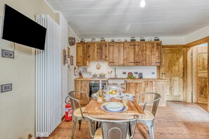 A kitchen with wooden cabinets, a dining table set with plates, glasses, and a bottle. - Luna Apartment Baita Ayana with Balcony Views, Oulx, Italy (Oulx)