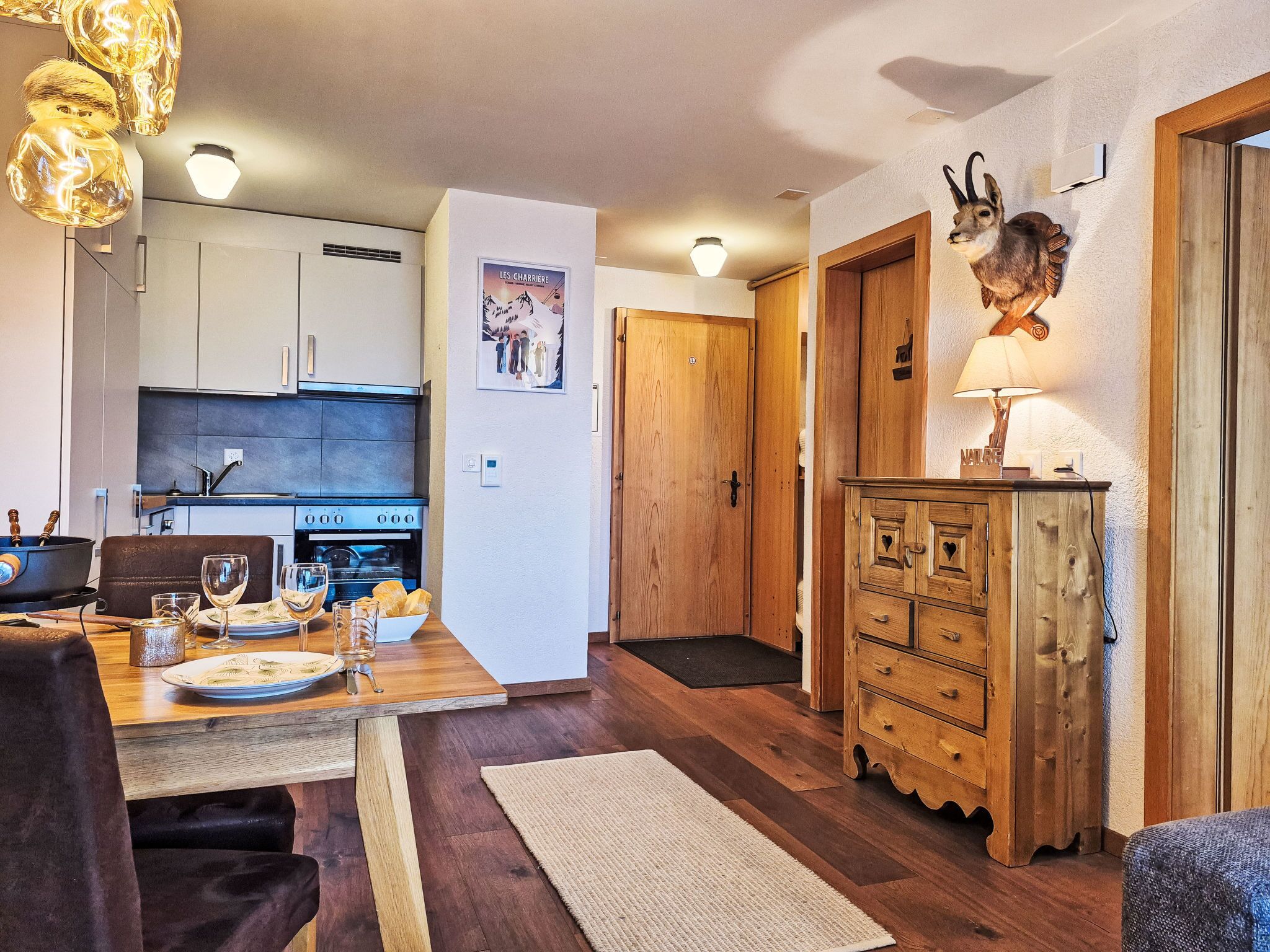 A cozy kitchen with wooden cabinets, a dining table set with plates and glasses, and a rustic wooden cabinet with a lamp.