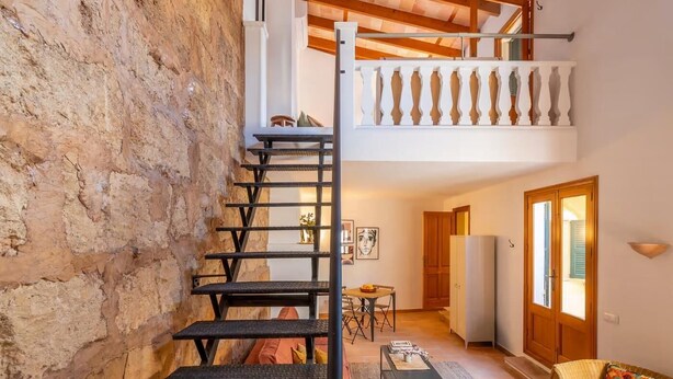 Een trap die leidt naar een slaapkamer op een entresol, met een balkon, een eethoek en een woonruimte met een bank en een vloerkleed.