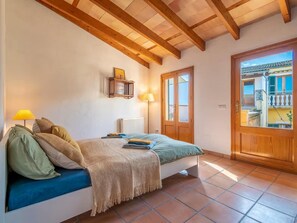 A bedroom with a bed, a wooden door, a window, and a radiator. - Casa Jutta: Charming Retreat with Terrace, WiFi & AC (Santa Margalida)
