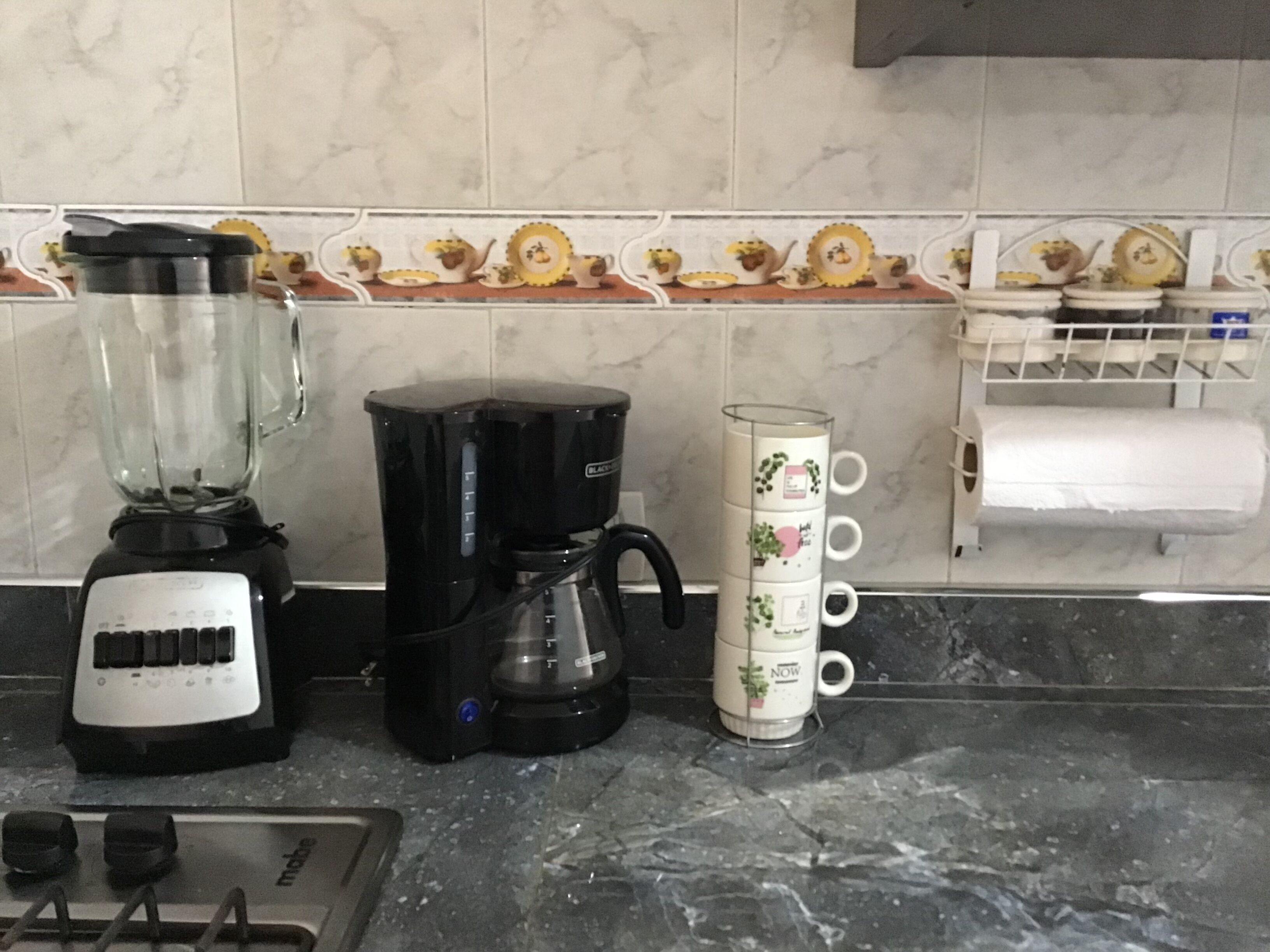 A kitchen with a blender, coffee maker, and a stack of white mugs on the counter.