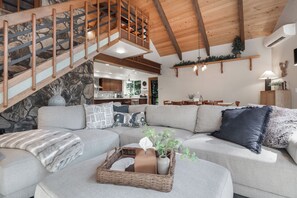 A spacious living area with a large sectional sofa, a wooden staircase, and a stone wall. - Northern 88 - Modern Mountain Retreat - Main Floor Master + Hot Tub + Firepit (Ronald)