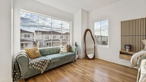 A modern living room with a grey sofa, wooden flooring, large windows, and a wooden wall panel. - Prime World Cup Access • Sleeps 8 - 10 • New Luxury Build (Dallas)