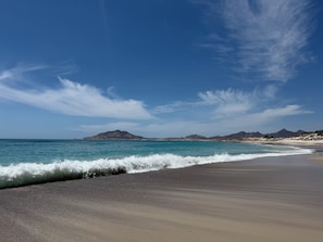 A beach with clear skies, waves, and distant mountains.