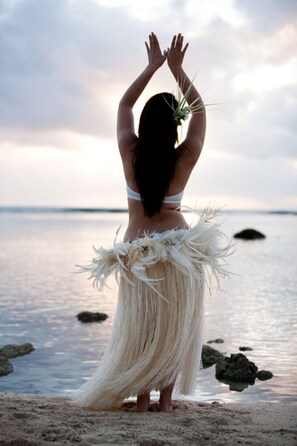 A person standing on a beach with a body of water and rocks in the background.