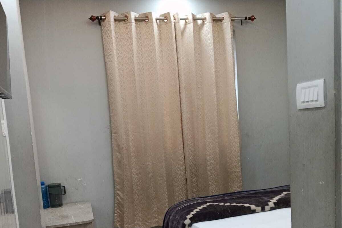 Un dormitorio con cama, mesita de noche, ventilador de techo y ventana con cortinas.