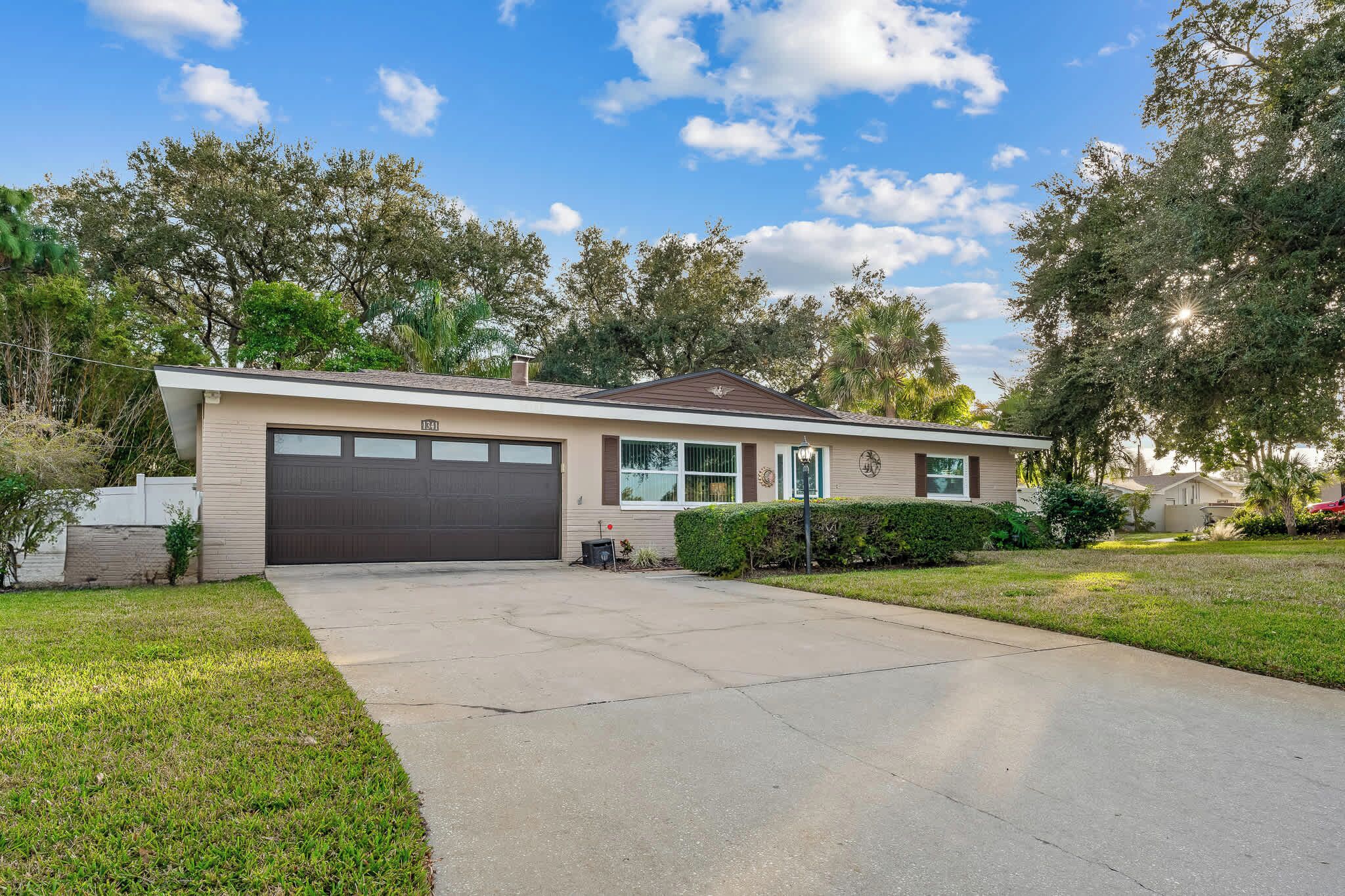A single-story house with a garage, a front lawn, and mature trees in the background.