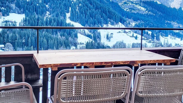 Eine Terrasse mit Holztisch und Korbstühlen mit Blick auf eine verschneite Berglandschaft.