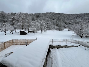Eine verschneite Landschaft mit Holzzaun, Steinmauer und einer kleinen Holzhütte.