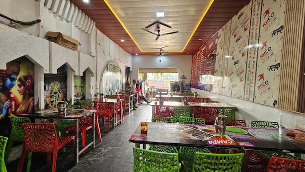 Un restaurante con sillas de plástico rojas y verdes, un ventilador de techo y paredes decoradas con carteles.