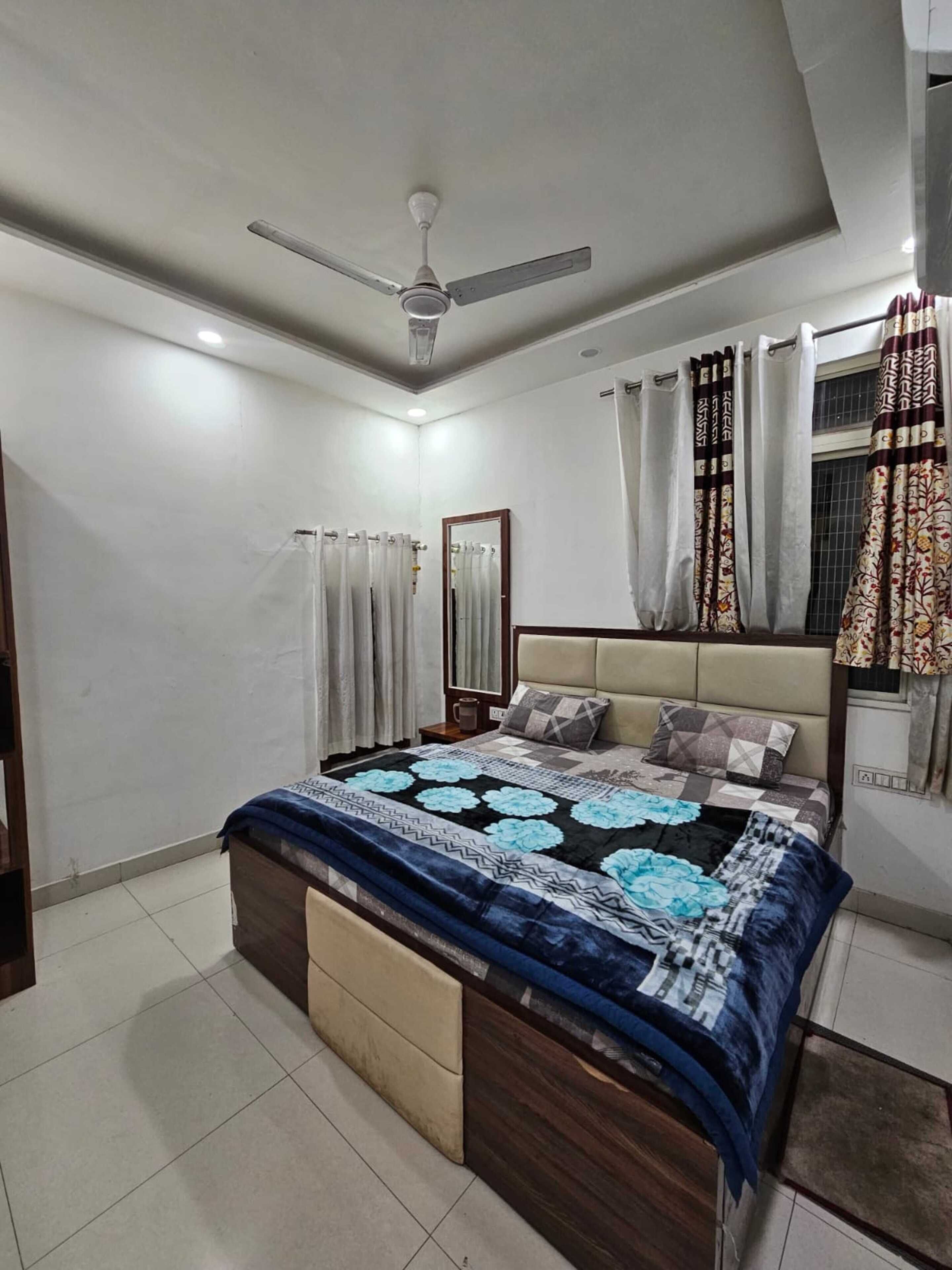 A bedroom with a bed, a ceiling fan, a window with curtains, and a tiled floor.