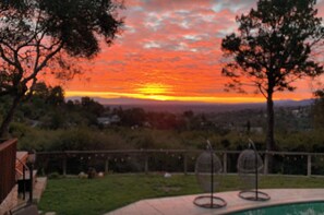 Vista al atardecer desde un patio trasero con piscina y comedero para pájaros.
