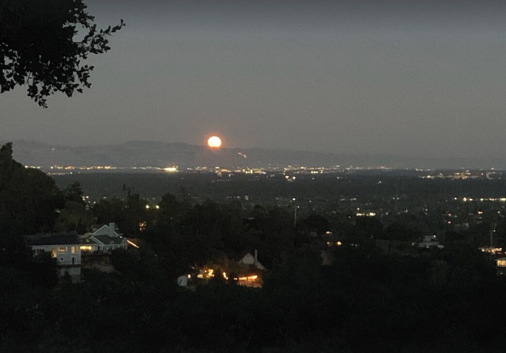 A cityscape at dusk with a visible sun setting over distant mountains.