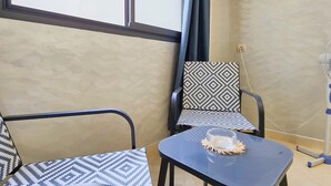 Una stanza con due sedie, un tavolo, una finestra con tende e un ventilatore a parete.