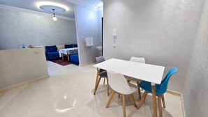 Zona pranzo moderna con tavolo bianco e sedie blu, un divano blu e un tavolino con tovaglia fantasia.