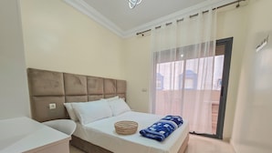 Una camera da letto con un letto, un comodino, una finestra con tende e un pavimento piastrellato.