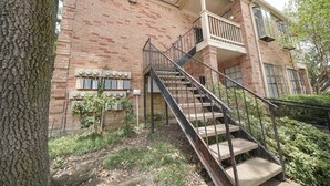 Ein Backsteinhaus mit einer zentralen Treppe, einem Balkon und einem kleinen Baum davor.