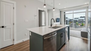 A modern kitchen with a central island, stainless steel appliances, and pendant lighting. - Eclectic New Condo in Seton’s hub (Calgary)