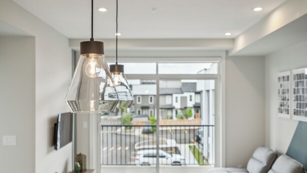 A modern living room with a sofa, a wooden side table, and a hanging light fixture. - Eclectic New Condo in Seton’s hub (Calgary)