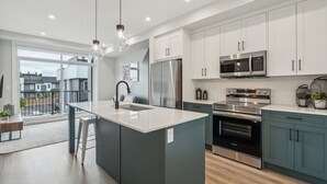 A modern kitchen with a large island, stainless steel appliances, and a view to the outside. - Eclectic New Condo in Seton’s hub (Calgary)