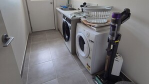A laundry room with a washing machine, dryer, and a vacuum cleaner. - Golden Beach Holiday Home (Golden Beach)
