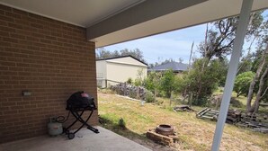 A covered patio area with a concrete floor, a brick wall, and a barbecue grill. - Golden Beach Holiday Home (Golden Beach)