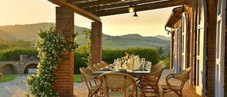 An outdoor dining area with a brick pergola, wicker chairs, and a table set for a meal.