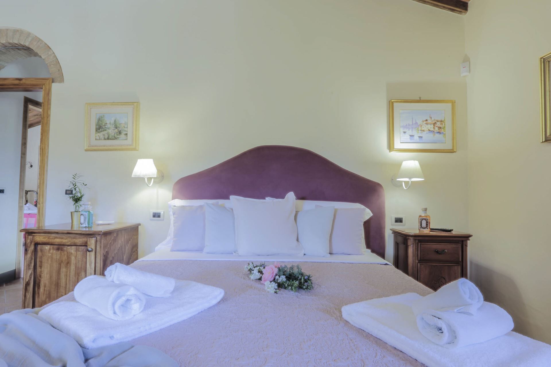 A hotel room with a large bed, two bedside tables, a mirror, and two framed pictures on the walls.